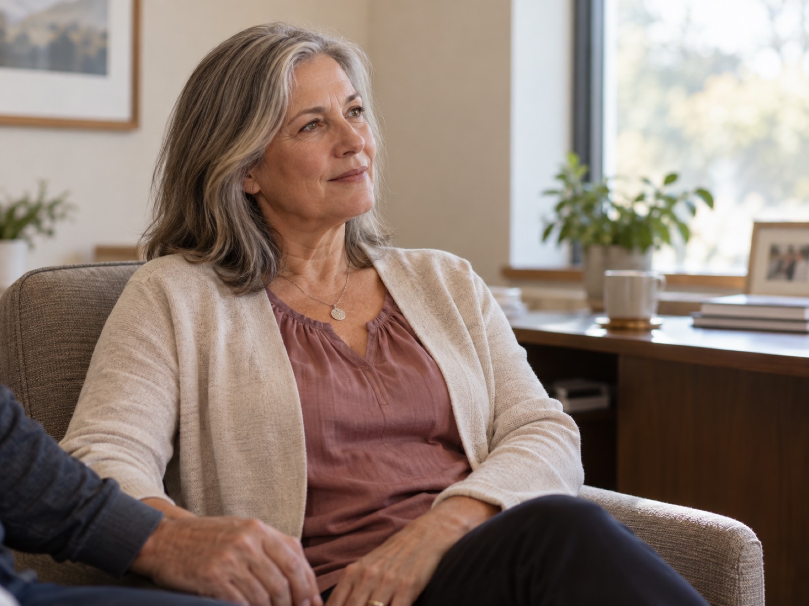 Woman sitting calmly in a warm consultation room with a partner's supportive hand beside her.